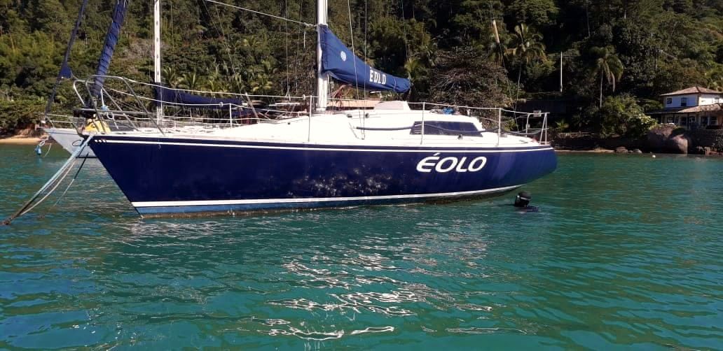 O veleiro Éolo, de casco azul-marinho, fundeado em águas verdes